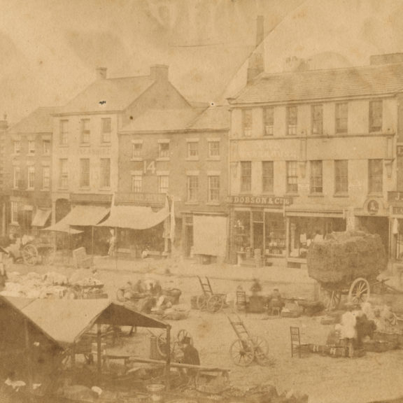 Images shows flag market as it was in 1853. The front of the Harris is where the row of shops is today. Old fashioned sepia image with stall holders and traders.