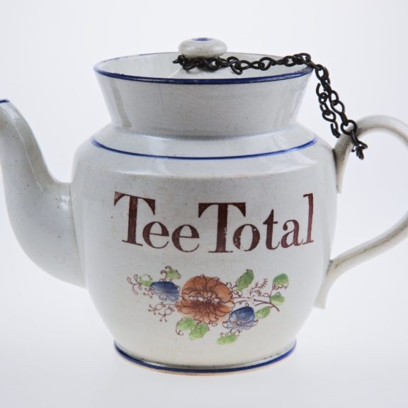 White tea pot with the words 'Tee Total' and decorative flowers on it.