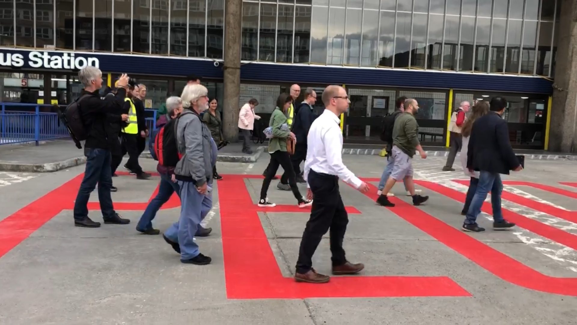 Image shows people walking over a large red sign that says 'People' painted on Preston bus station ground.