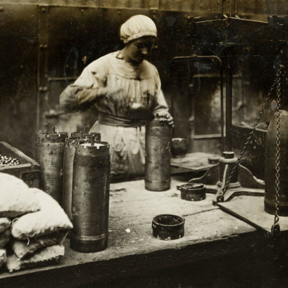 Lady working in factory filling metal shell that will be used for war.