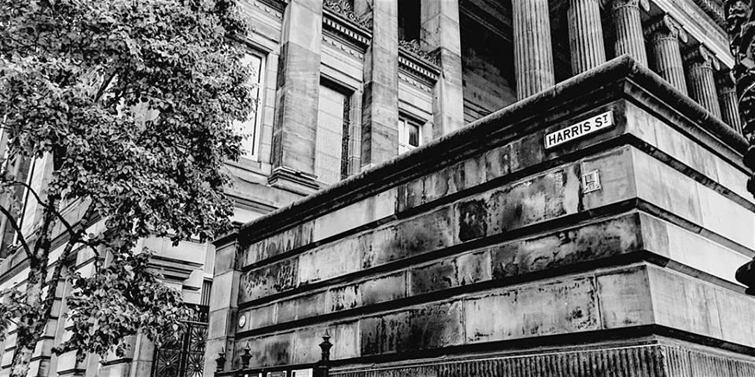 black and white image of the front corner of the harris building and road sign that says harris street