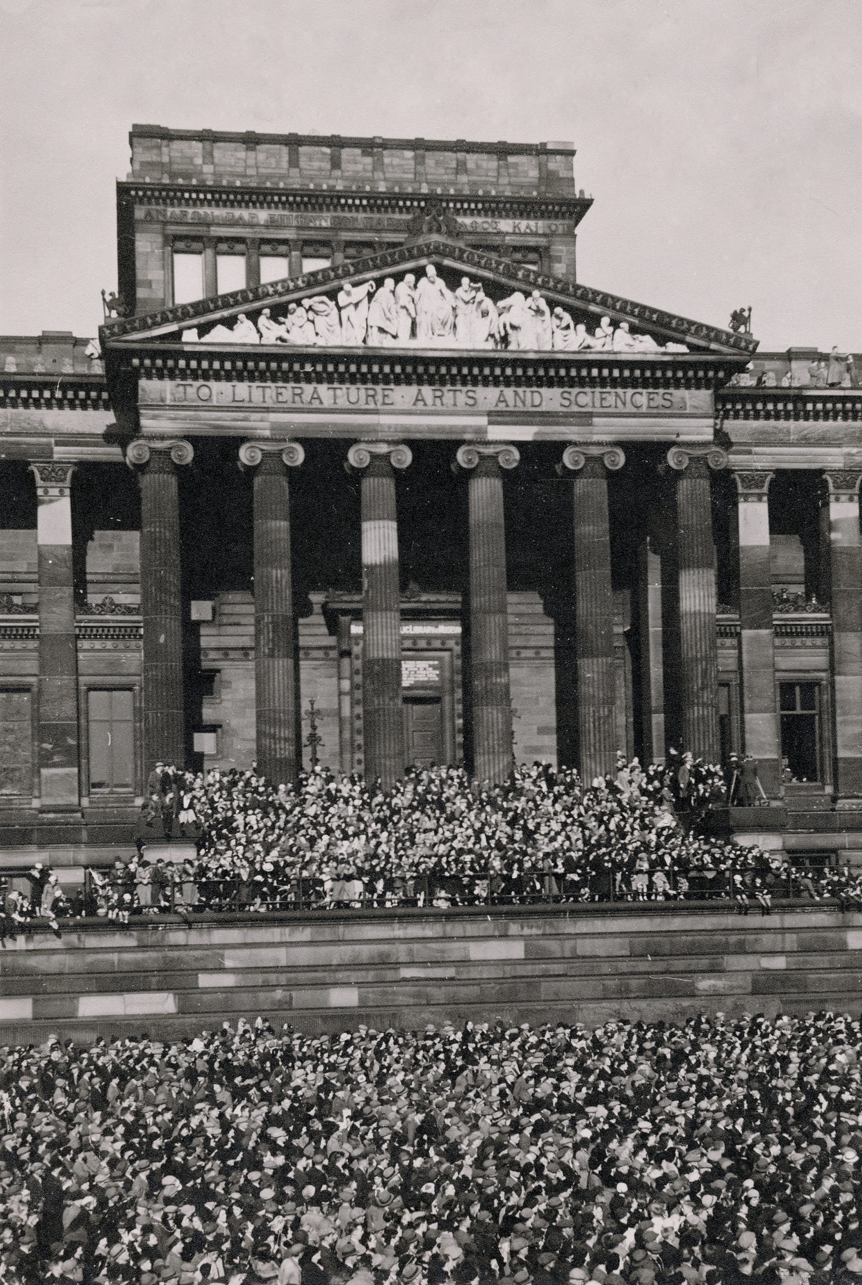 Old photo from the 40s of Preston flag market filled with a crows. Crowd is looking up at Harris Museum balcony which is also filled with people celebrating and listening to a speech