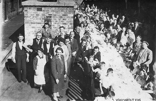 Long table with approximately 60 people sat down in the street at the table looking happy. 