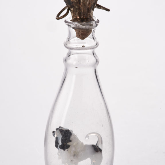 Small clear novelty scent bottle with cork lid containing a minature black and white dog figure