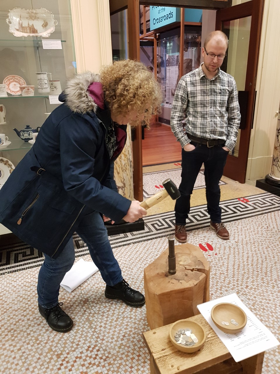 One of the tour members striking their own Viking Cuerdale coin with a mallet watched by the History curator