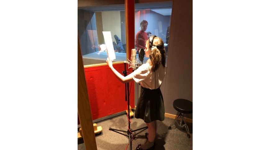 Primary school aged girl recording voice over in studio with head phones on.