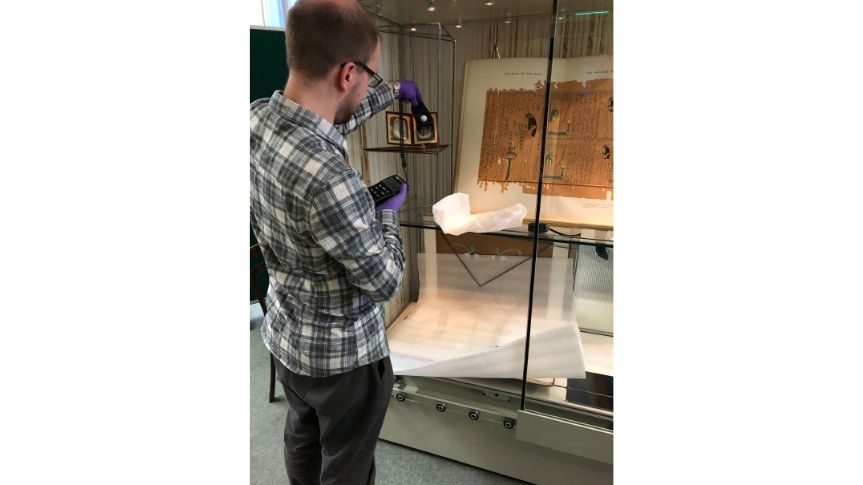 Photo of History Curator setting light levels in cabinet that houses daguerreotype and old Egyptian books. James is using a small electrical device to do this.