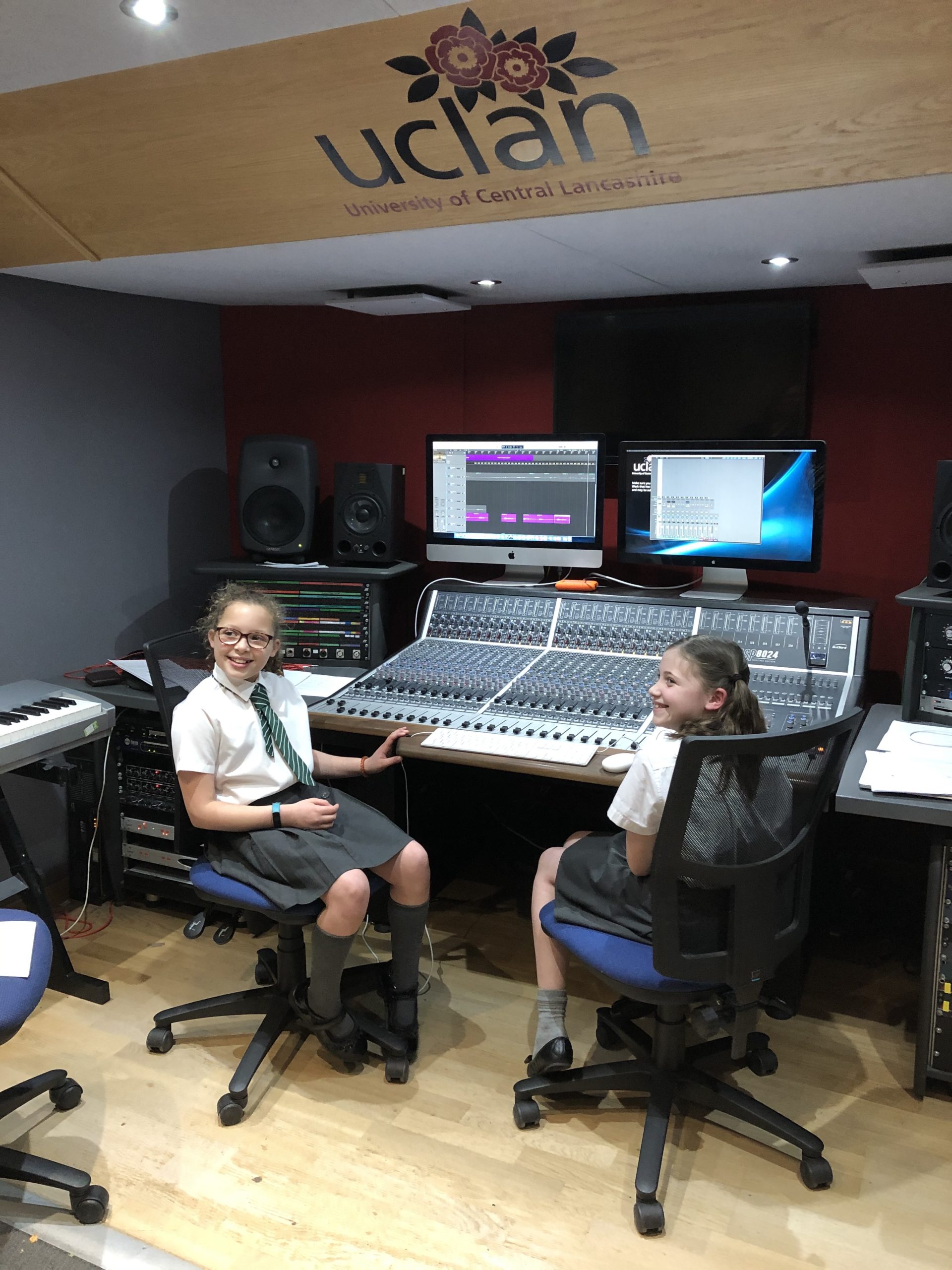 Two primary school aged children in a recording studio sat at a sound desk, smiling 