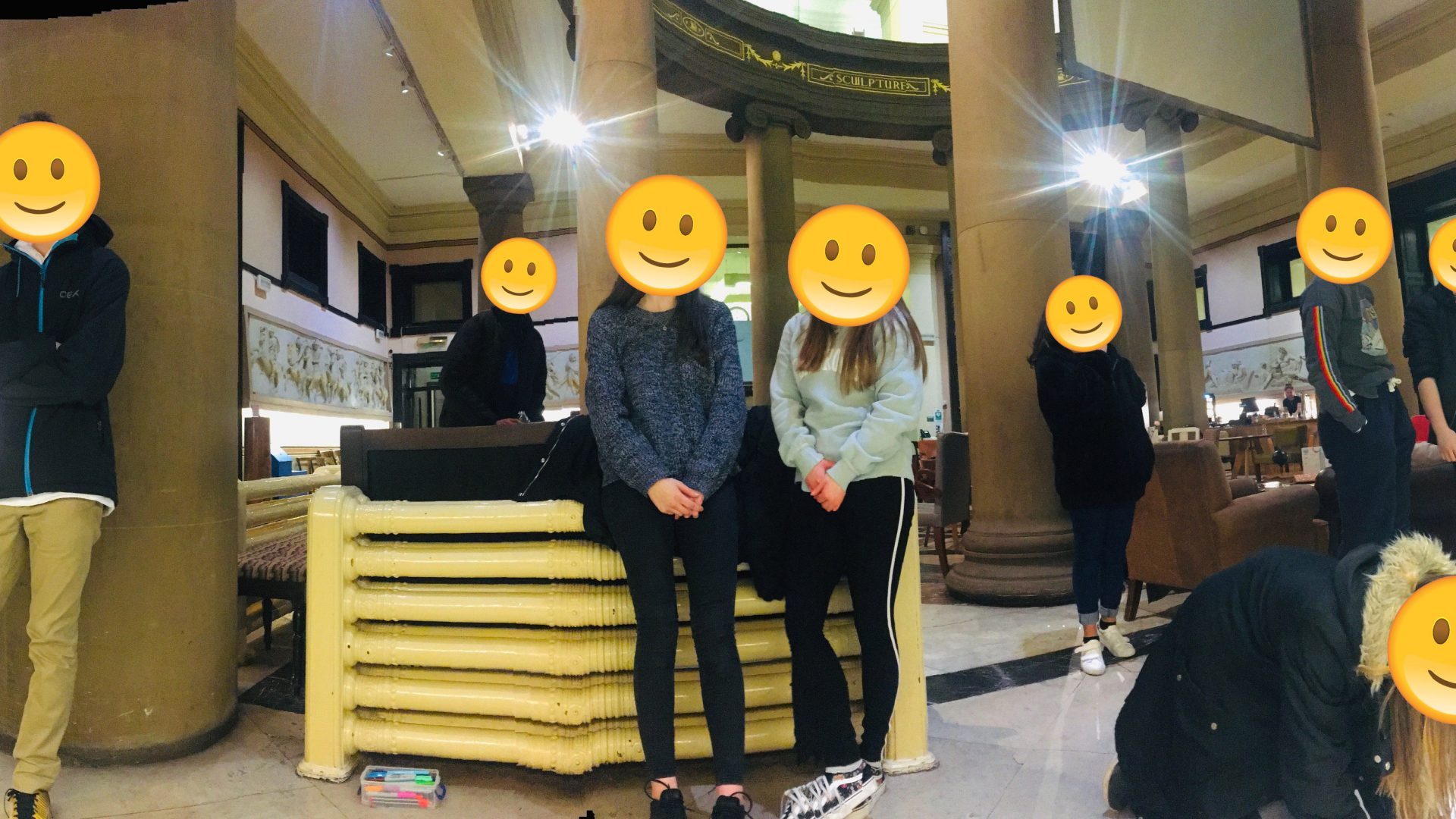 Group of young people stood in Harris Cafe - all of their faces are covered with a smiley face emoji.