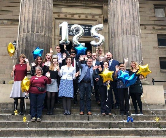 Staff stood on the front balcony of the Harris waving, holding 125 year balloons