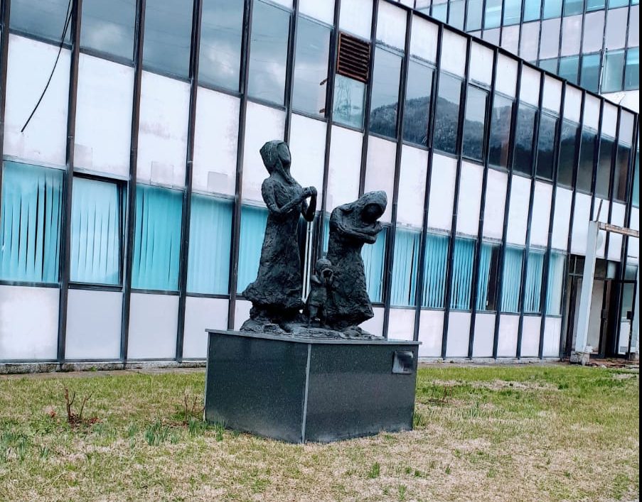 Photo of 2 female statue figures with a small toddler stood inbetween them. The first figure is looking up to the sky and the second is hunched over holding her arms.