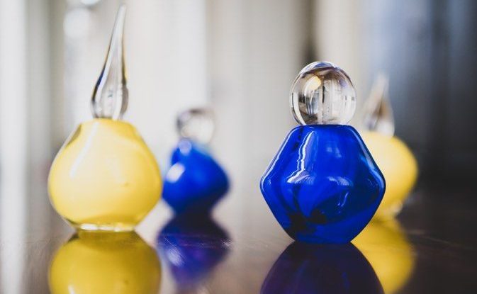 Image shows 4 small bottles, 2 made of yellow glass and 2 made of blue glass. They are in different shapes with clear glass lids.