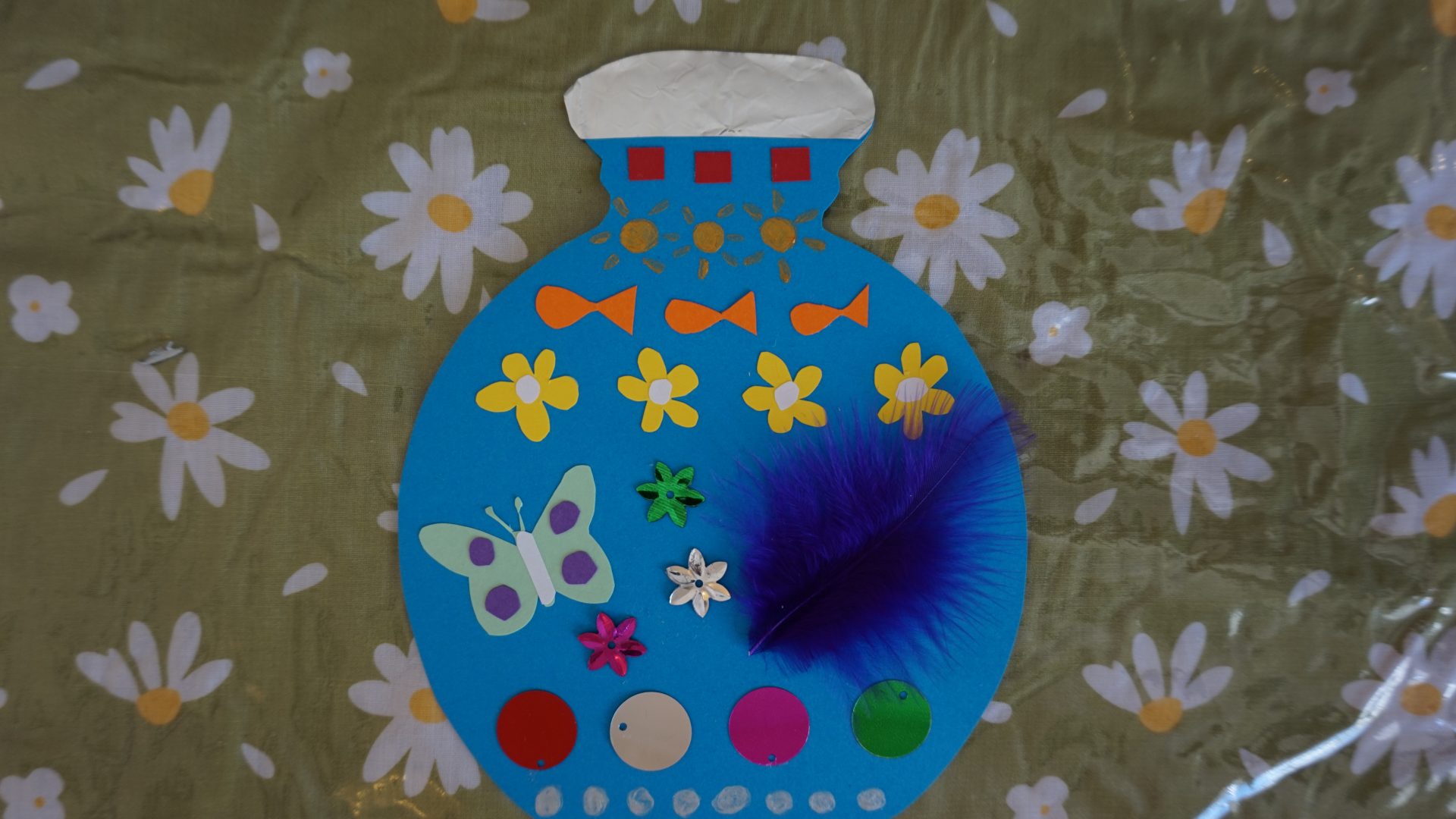 A card bottle decorated with colourful paper, feathers and sequins