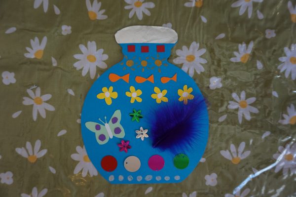 A card bottle decorated with colourful paper, feathers and sequins