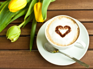 A cup of coffee with a heart and some yellow tulips