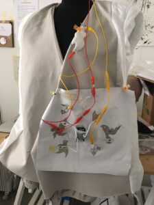 Image of Nicola Woodham's white soundsuit with exposed red and yellow wires created for the Buffer performance.