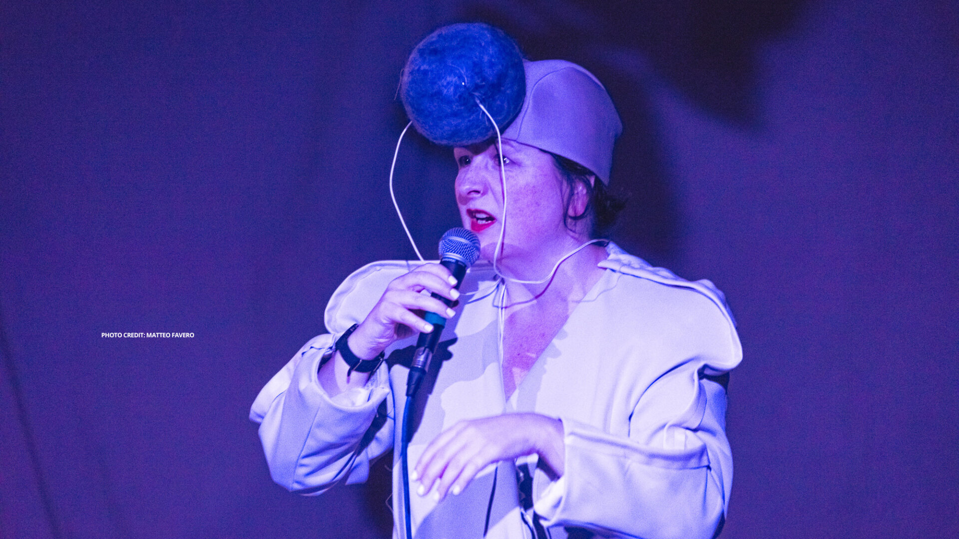 Image of Nicola Woodham during their performance of Buffer at Cafe Oto. Nicola is wearing a custom made white soundsuit and holding a microphone.