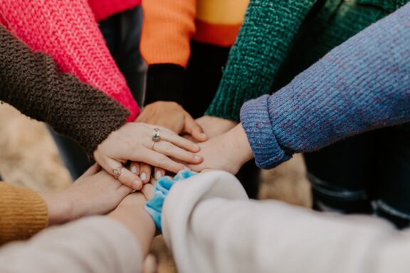 Community image with seven hands stacked together in the middle