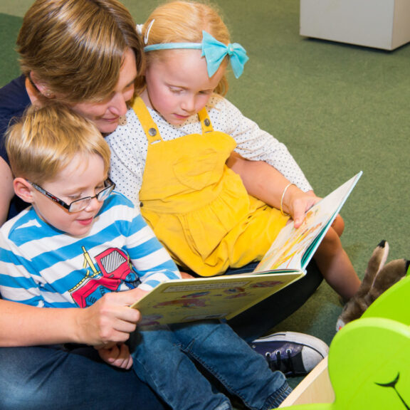 An image of two children reading with their Mother