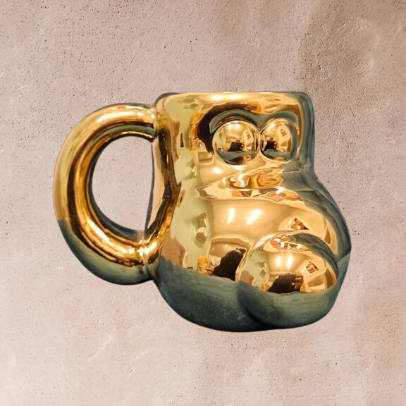 A golden gromit mug with clay in the background.