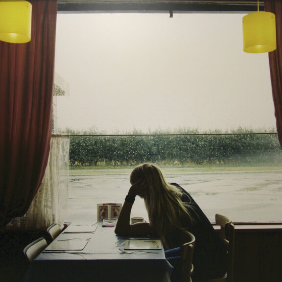 Starkey’s photograph shows a woman sat at a table with her hand resting on her head looking outside the window at roadside cafe