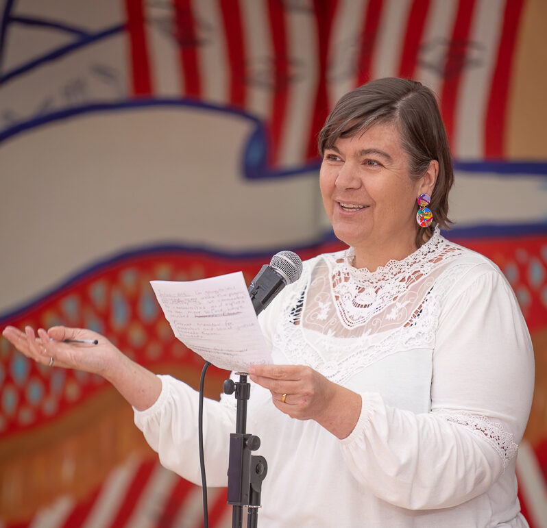 Image of a person standing holding a piece of white paper making a speech into a microphone