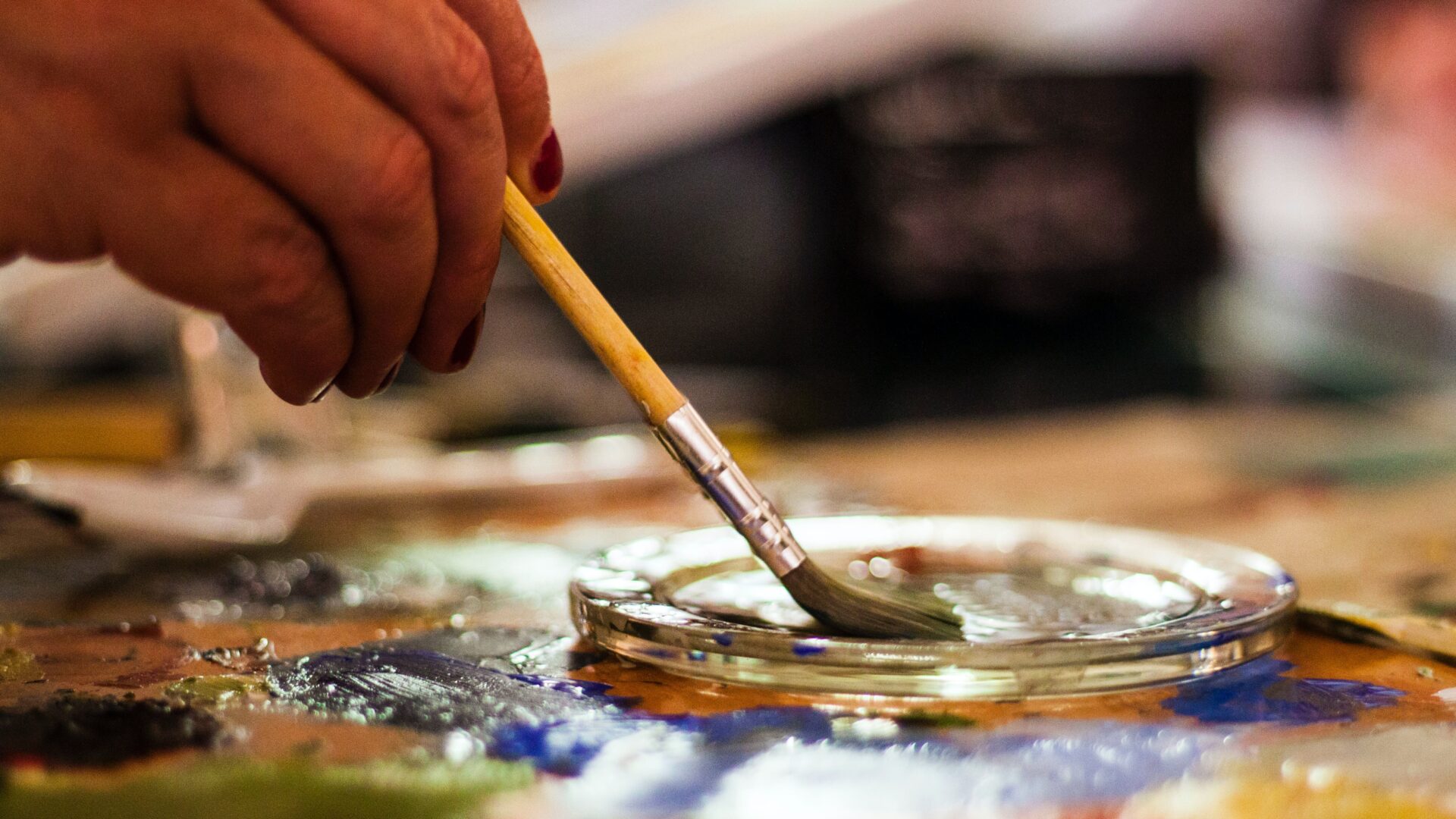 A person dips a paint brush into a glass tray.