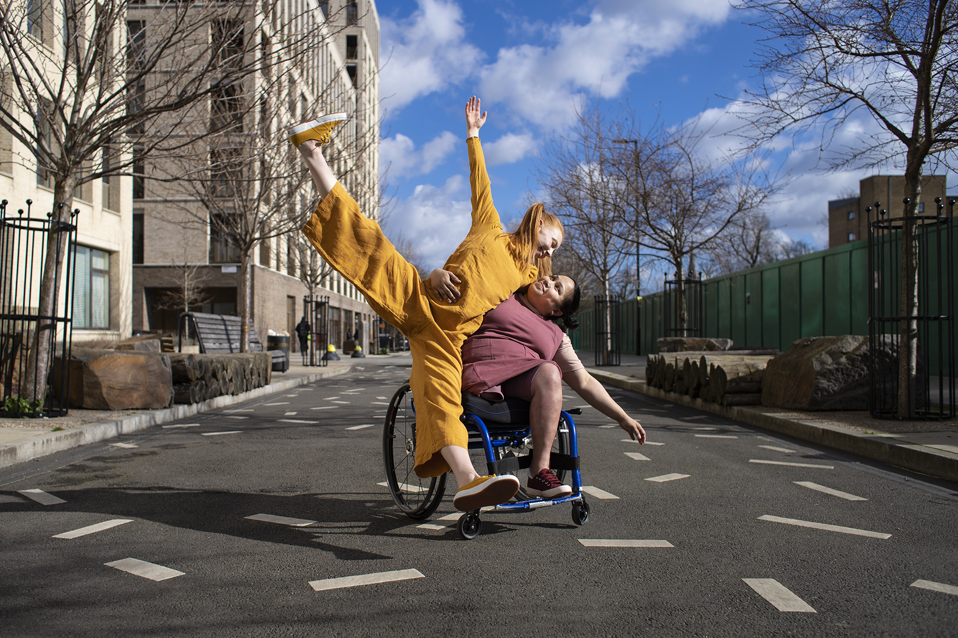 Image of a person in a star shape supported by a person in a wheelchair in a empty street,