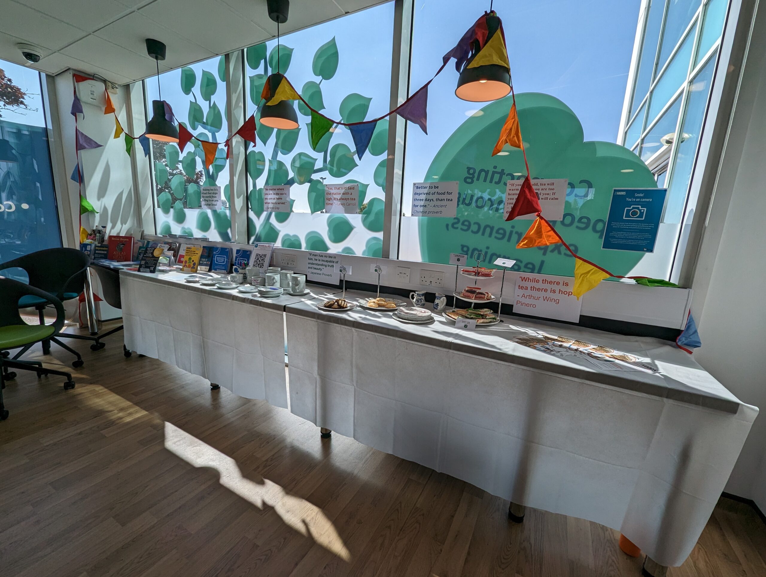 The tea display at Lancashire Recovery Collage. It features colourful bunting, a long table, cups and saucers, and famous quotes about tea on pieces of paper.
