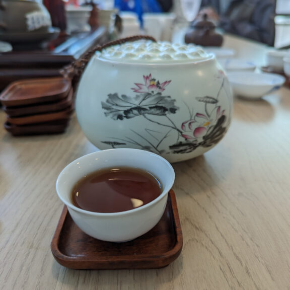 A small saucer of tea and a decorated tea pot.