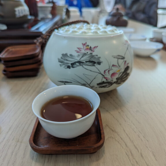 A small saucer of tea and a decorated tea pot.