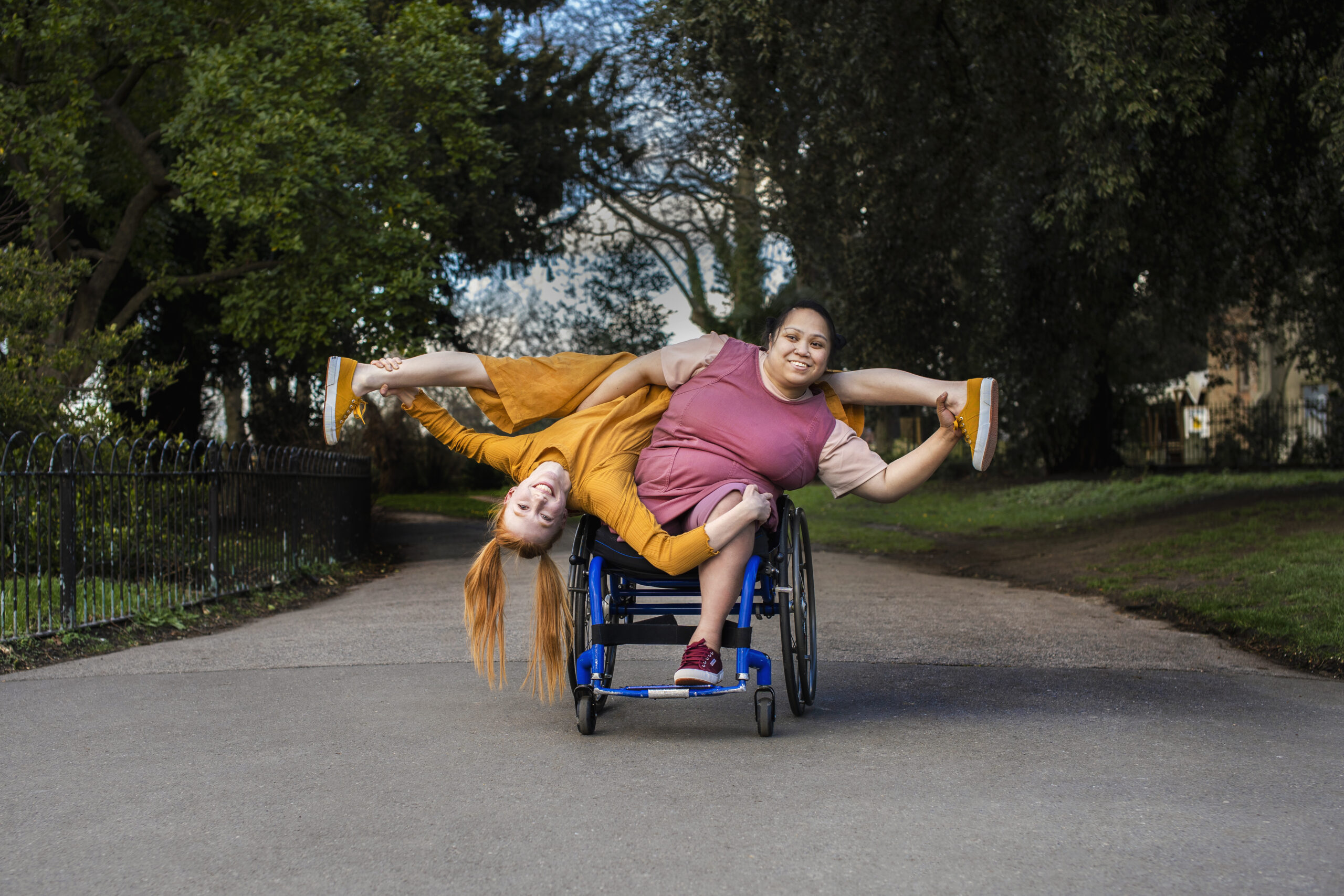 A person in a wheelchair supports another person who is leaning against them upside down.