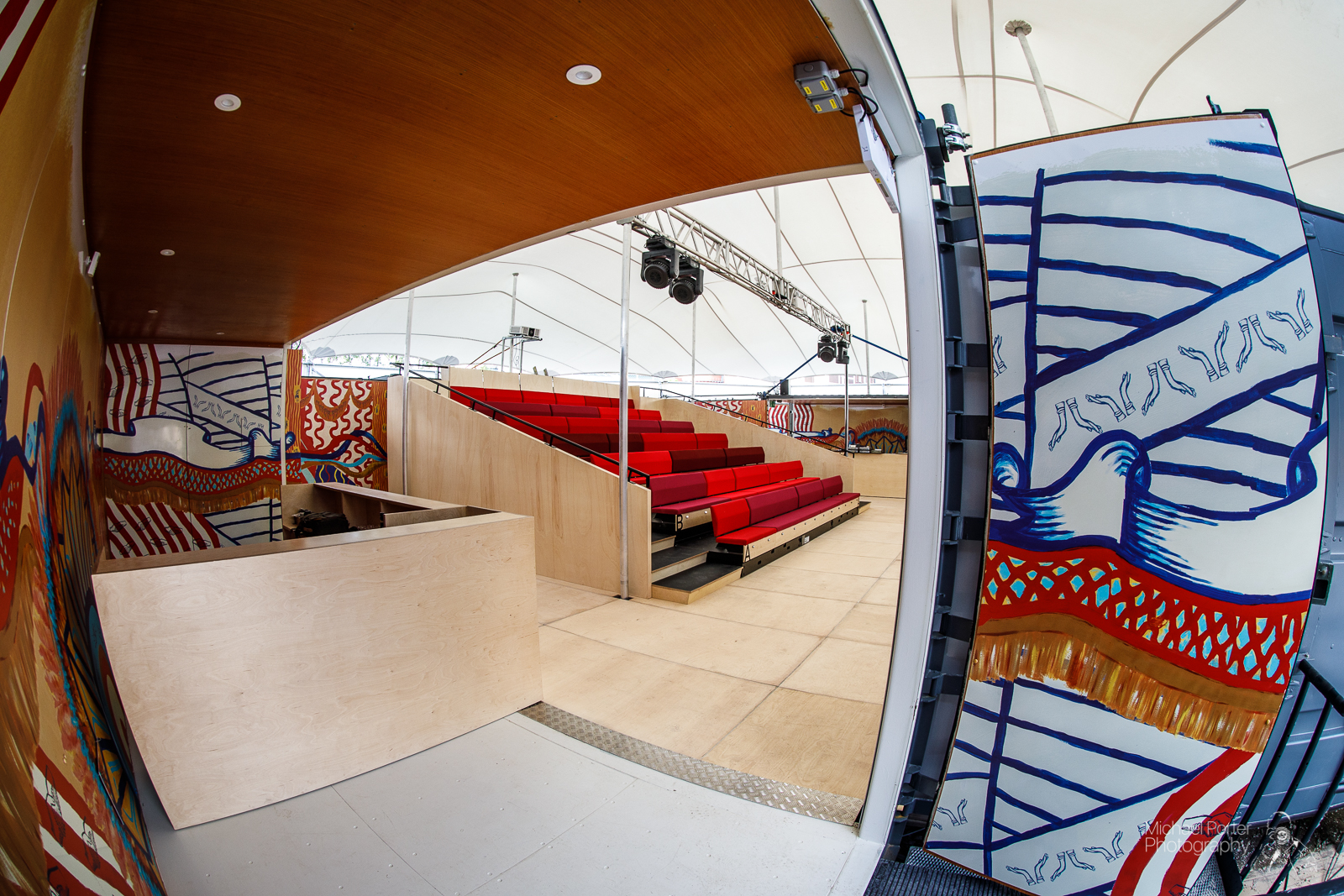 The inside of the mobile event tent. Red seating is visible and the walls have been painted with colourful patterns.