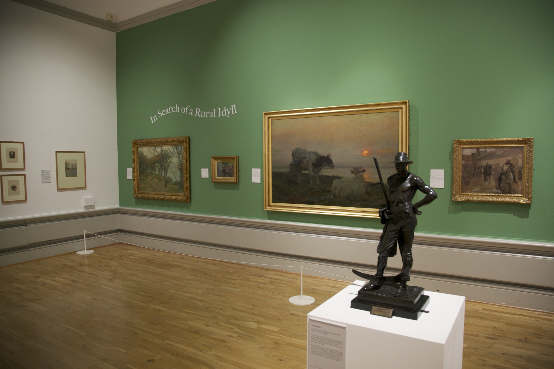 Landscape paintings hung on a green wall behind a small statue.