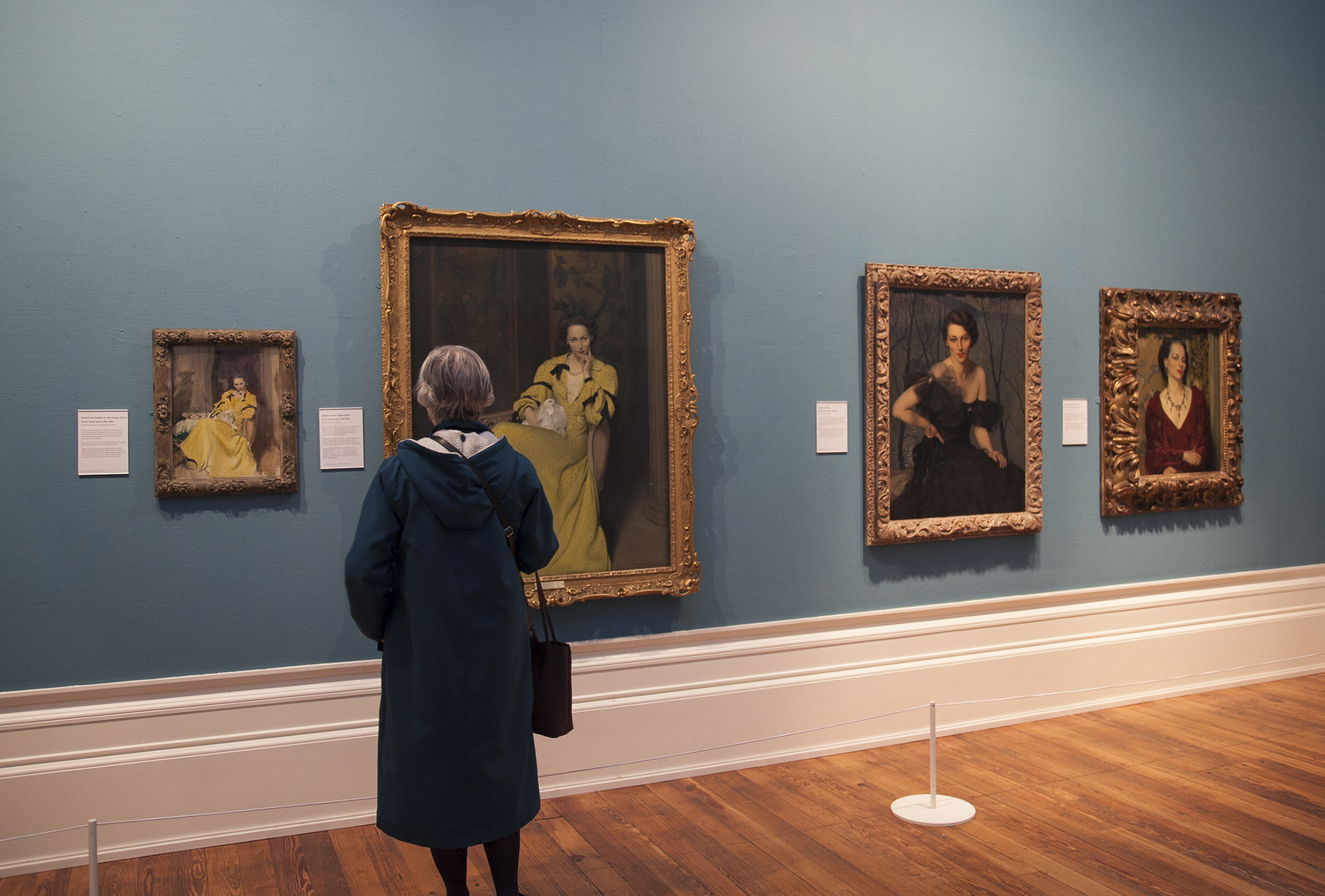 A person stands looking at the painting of Pauline in a Yellow Dress.
