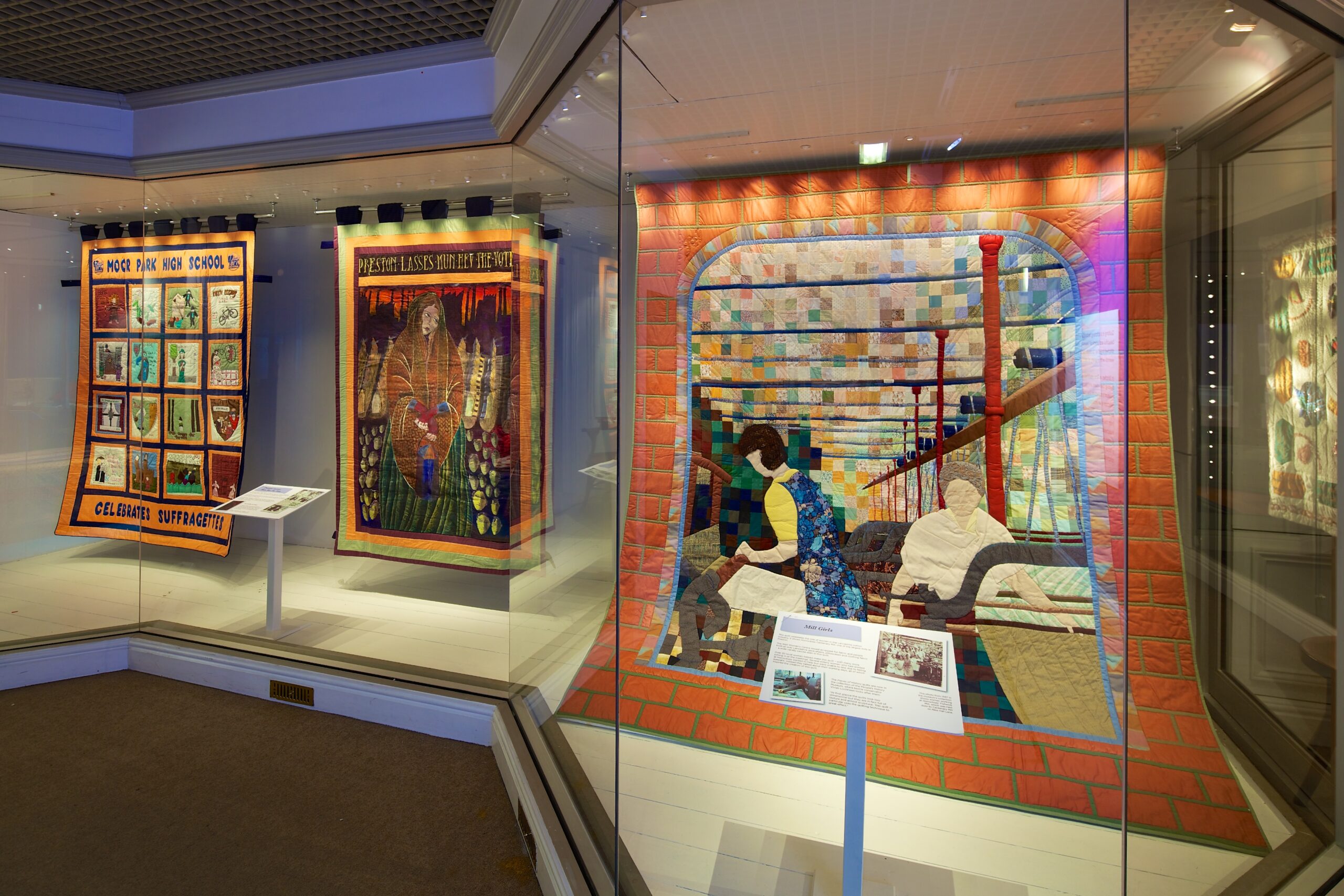 Three quilted banners hang in a display case.