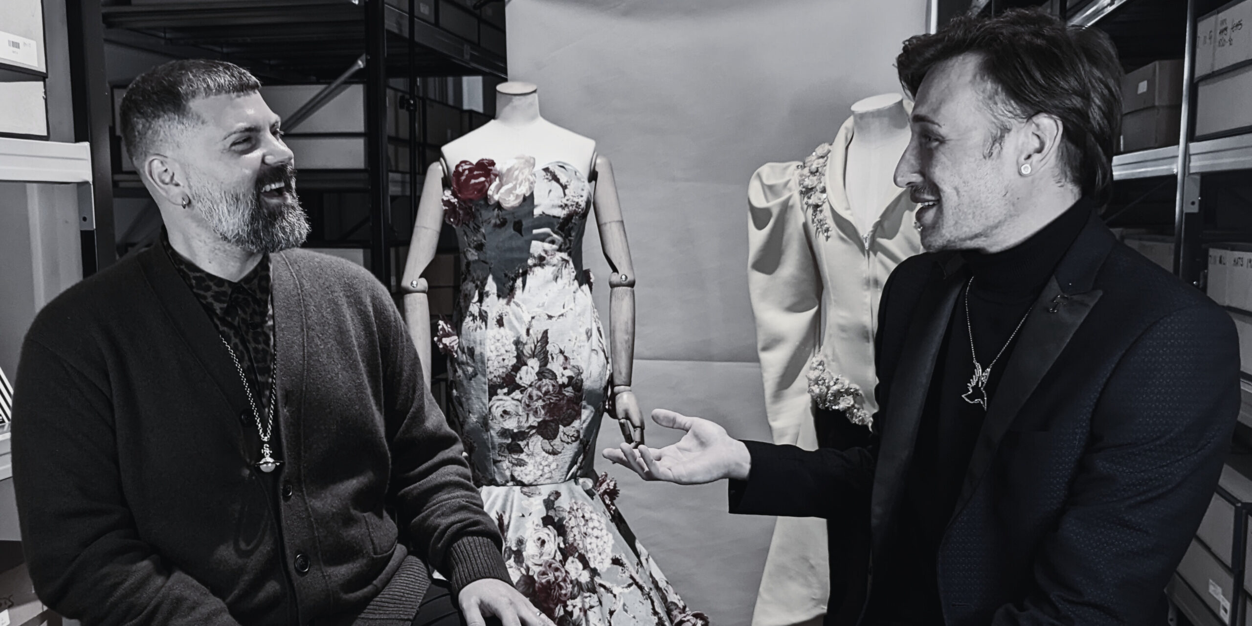 A black and white image of two people sitting in front of costumes and laughing.