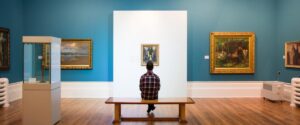 Image of a person sat in a gallery surrounded by paintings