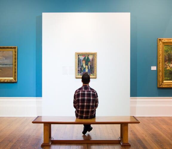 Image of a person sat in a gallery surrounded by paintings