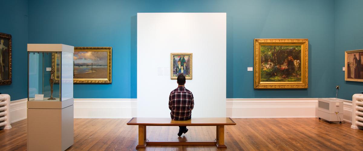 Image of a person sat in a gallery surrounded by paintings