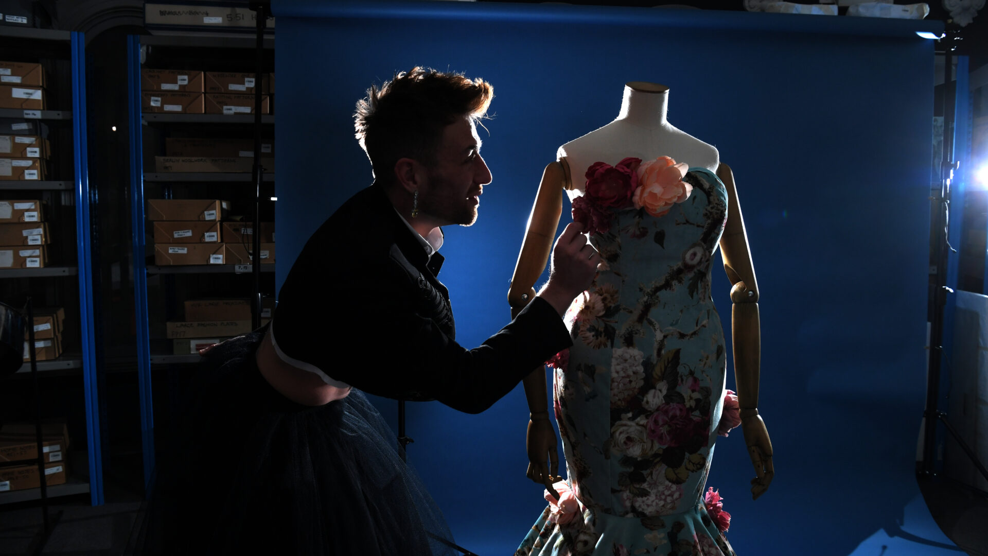 A person in a black jacket adjusts the roses decorating a blue dress.