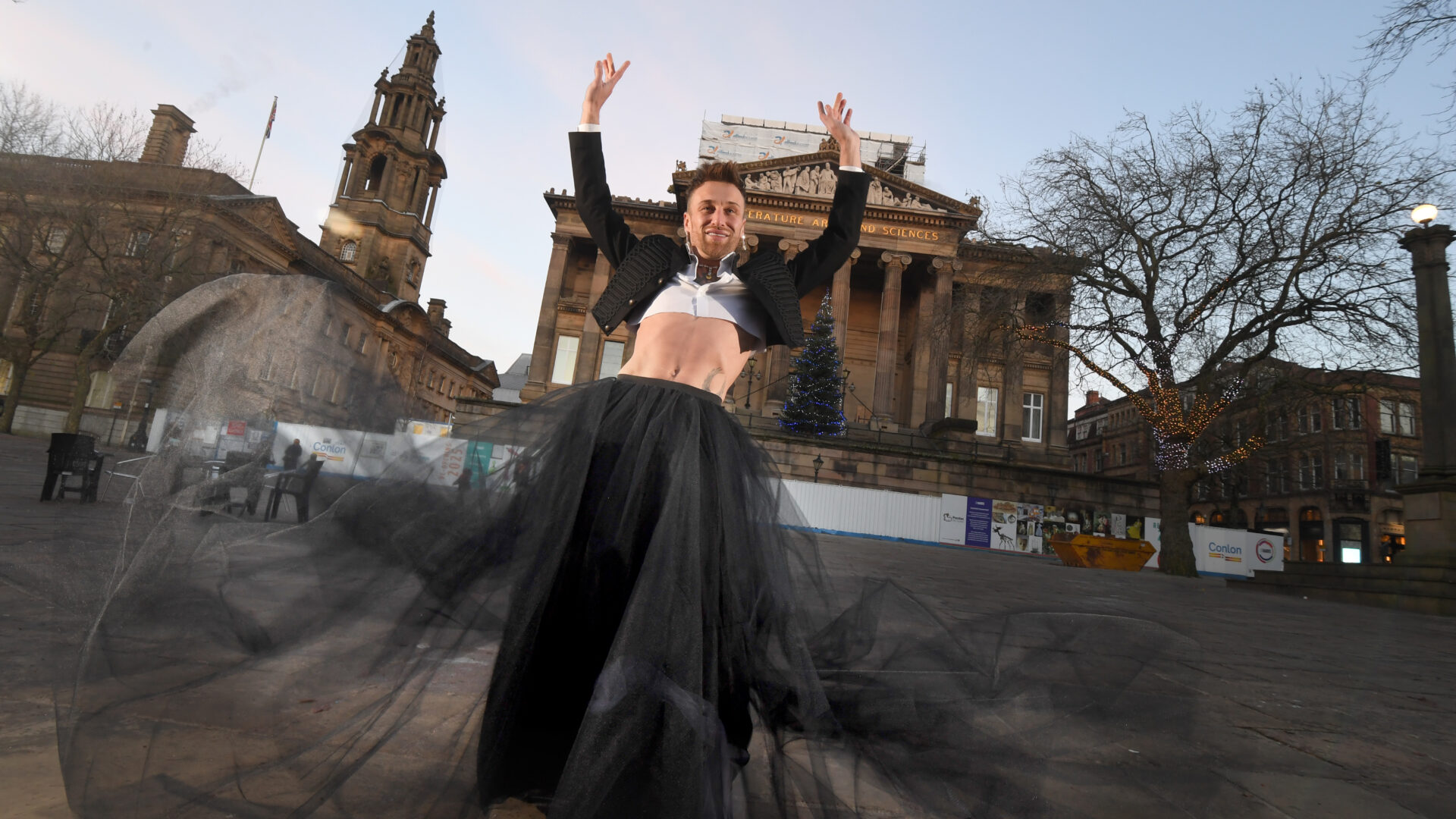 A person wearing a cropped jacket and a long black skirt stands in front of the Harris on the flag market.