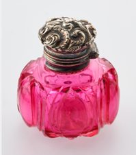 A small pinkish-red glass bottle with bronze cap.
