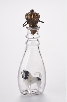 A clear class bottle containing a black and white dog figurine.