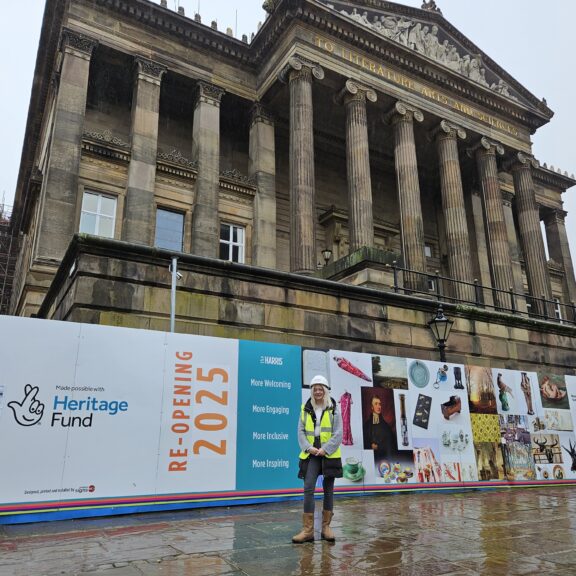 A person wearing a hard hat and high vis jacket stood in front of the Harris building.