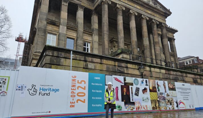A person wearing a hard hat and high vis jacket stood in front of the Harris building.