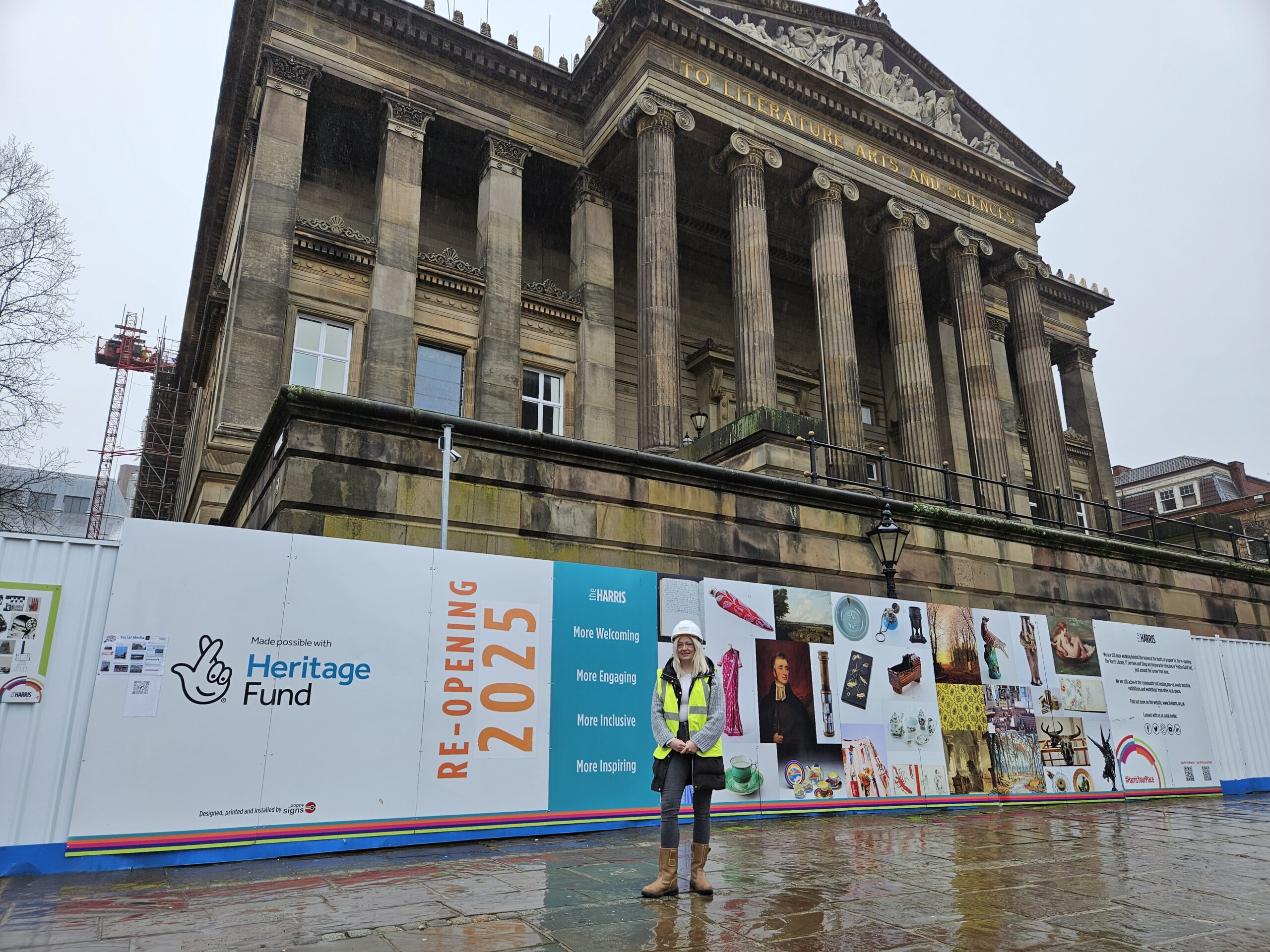 A person wearing a hard hat and high vis jacket stood in front of the Harris building.