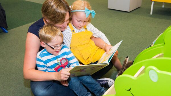 A parent reading a book with two young children.