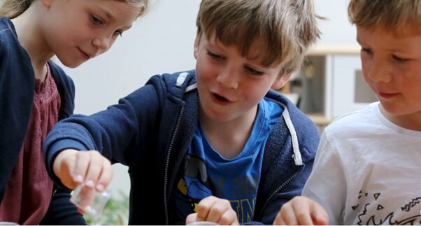 Three young children looking at a small clear object.