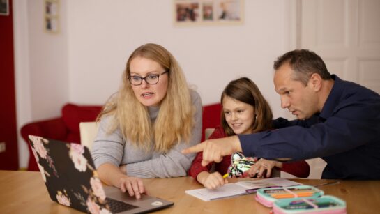 Image of a woman and a man sat round a computer pointing with a young child.